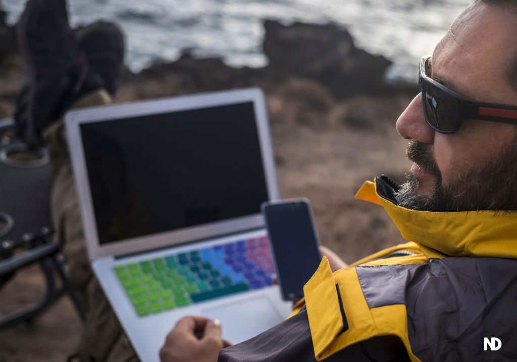 Hombre trabaja en su computador telefono al aire libre nomada digital