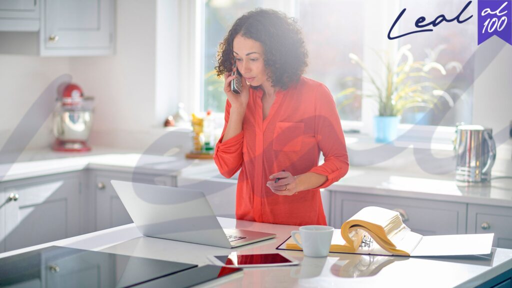 Mujer habla por teléfono frente a computador portatil en cocina luz día Visa Nómada Digital en España nómadas digitales